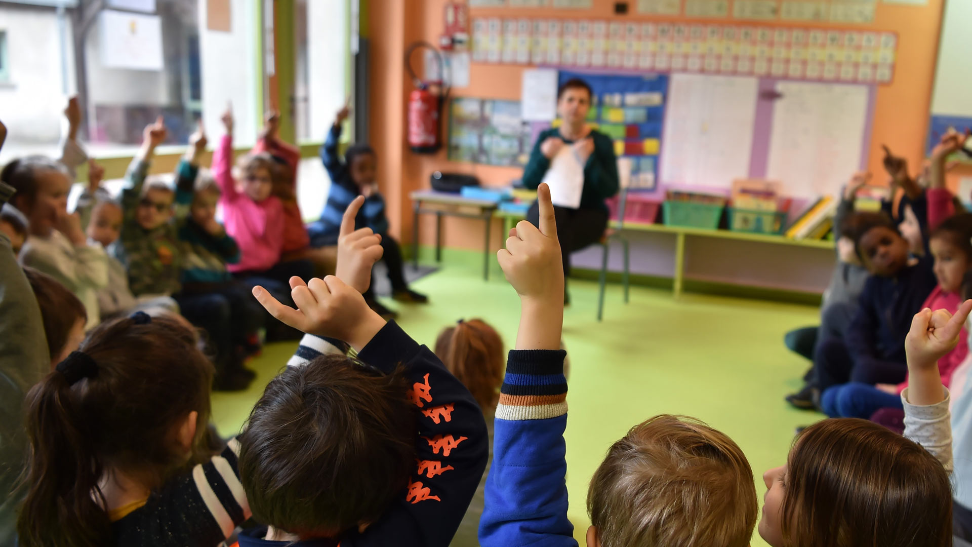 Des écoliers levant le doigts dans une salle de classe