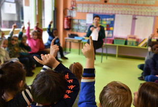 Des écoliers levant le doigts dans une salle de classe